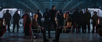 Movie still from “Fast & Furious Presents: Hobbs & Shaw” (2019), directed by David Leitch – A group of men sitting on chairs in a room; Wide shot, High angle