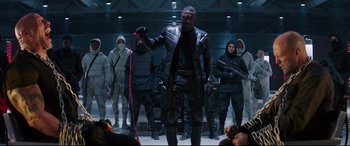 Movie still from “Fast & Furious Presents: Hobbs & Shaw” (2019), directed by David Leitch – A group of men in black and white outfits; Wide shot, Over the shoulder angle