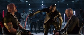 Movie still from “Fast & Furious Presents: Hobbs & Shaw” (2019), directed by David Leitch – A man in a black leather jacket holding a red whip; Medium shot, Over the shoulder angle