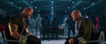 Movie still from “Fast & Furious Presents: Hobbs & Shaw” (2019), directed by David Leitch – A group of men standing next to each other holding guns; Medium shot, Over the shoulder angle