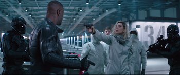 Movie still from “Fast & Furious Presents: Hobbs & Shaw” (2019), directed by David Leitch – A woman holding a gun pointed at a man in a white suit; Medium shot, Over the shoulder angle