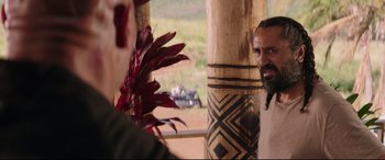 Movie still from “Fast & Furious Presents: Hobbs & Shaw” (2019), directed by David Leitch – A man standing next to a wooden pole with a plant on it; Close Up shot, Over the shoulder angle