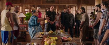 Movie still from “Fast & Furious Presents: Hobbs & Shaw” (2019), directed by David Leitch – A group of people standing around a table with fruit on it; Medium shot, Over the shoulder angle