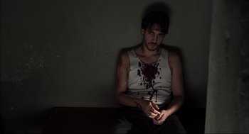 A young man with blood on his shirt sitting on the ground