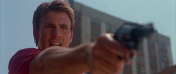 Movie still from “Cellular” (2004), directed by David R. Ellis – A person holding a gun with a building in the background; Close Up shot, Low angle