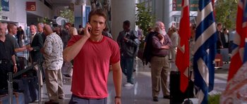 Movie still from “Cellular” (2004), directed by David R. Ellis – A young man is talking on a cell phone while standing in an airport; Medium shot, Over the shoulder angle