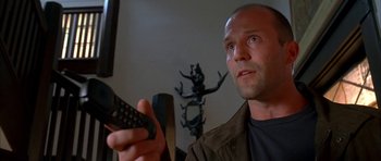 Movie still from “Cellular” (2004), directed by David R. Ellis – A man holding a remote control in front of a television; Close Up shot, Low angle