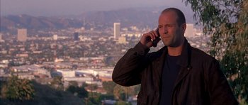 Movie still from “Cellular” (2004), directed by David R. Ellis – A man is talking on a cell phone in front of a city skyline; Medium shot, Low angle