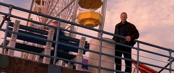 Movie still from “Cellular” (2004), directed by David R. Ellis – A man standing next to a metal railing near a ferris wheel; Wide shot, Over the shoulder angle