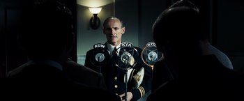 Movie still from “Changeling” (2008), directed by Clint Eastwood – A man in a uniform standing in front of microphones in a room; Medium shot, Low angle