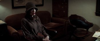 Movie still from “Changeling” (2008), directed by Clint Eastwood – A woman sitting in a chair wearing a hat and coat; Medium shot, High angle