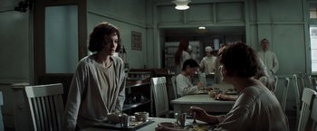 Movie still from “Changeling” (2008), directed by Clint Eastwood – A group of people sitting at a table in a room; Medium shot, Over the shoulder angle