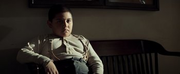 Movie still from “Changeling” (2008), directed by Clint Eastwood – A young boy sitting on a chair in a room; Medium shot, Low angle