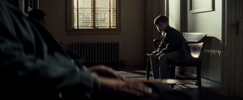 Movie still from “Changeling” (2008), directed by Clint Eastwood – A man sitting on a chair looking at a phone; Medium shot, Over the shoulder angle