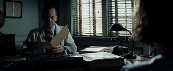 Movie still from “Changeling” (2008), directed by Clint Eastwood – A man sitting at a desk reading a piece of paper; Medium shot, Low angle
