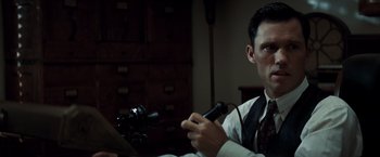 Movie still from “Changeling” (2008), directed by Clint Eastwood – A man sitting in front of a camera holding a game controller; Close Up shot, Low angle