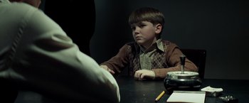 Movie still from “Changeling” (2008), directed by Clint Eastwood – A young boy sitting at a table with a pen and paper; Medium shot, Over the shoulder angle
