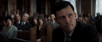 Movie still from “Changeling” (2008), directed by Clint Eastwood – A man in a suit and tie in front of a group of people; Close Up shot, Over the shoulder angle