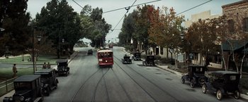 Movie still from “Changeling” (2008), directed by Clint Eastwood – A red trolley car traveling down a street past a row of trees; Extreme Wide shot, High angle