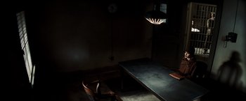 Movie still from “Changeling” (2008), directed by Clint Eastwood – A table and chair in a dark room with a clock on the wall; Wide shot, High angle