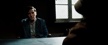 Movie still from “Changeling” (2008), directed by Clint Eastwood – A man sitting at a table in front of a window; Medium shot, Over the shoulder angle