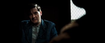 Movie still from “Changeling” (2008), directed by Clint Eastwood – A man in a blue jacket is sitting in a dark room; Close Up shot, Over the shoulder angle