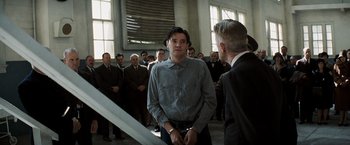 Movie still from “Changeling” (2008), directed by Clint Eastwood – A group of people in a room with a man standing in front of them; Medium shot, Low angle