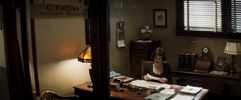 Movie still from “Changeling” (2008), directed by Clint Eastwood – A woman sitting at a desk in an office reading papers; Medium shot, High angle