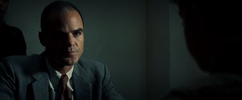Movie still from “Changeling” (2008), directed by Clint Eastwood – A man wearing a suit and tie sitting in front of a wall; Close Up shot, Low angle