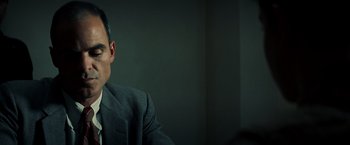 Movie still from “Changeling” (2008), directed by Clint Eastwood – A man wearing a suit and tie sitting in front of a wall; Close Up shot, Low angle