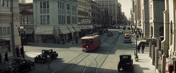 Movie still from “Changeling” (2008), directed by Clint Eastwood – A red train traveling down the tracks in a city; Extreme Wide shot, High angle
