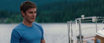Movie still from “Charlie St. Cloud” (2010), directed by Burr Steers – A man in a blue t - shirt standing next to a body of water; Medium shot, Over the shoulder angle