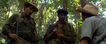 Movie still from “Che: Part One” (2008), directed by Steven Soderbergh – Two men in the woods looking at a cell phone; Medium shot, Low angle