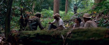 Movie still from “Che: Part One” (2008), directed by Steven Soderbergh – A group of men sitting on a log in the woods; Wide shot, High angle