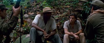Movie still from “Che: Part One” (2008), directed by Steven Soderbergh – Two men sitting on the side of a forest; Medium shot, Low angle