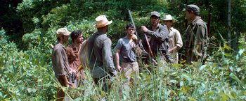 Movie still from “Che: Part One” (2008), directed by Steven Soderbergh – A group of men standing in the grass; Medium shot, Over the shoulder angle