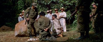 Movie still from “Che: Part One” (2008), directed by Steven Soderbergh – A man kneeling down in front of a group of people; Wide shot, Over the shoulder angle
