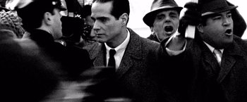 Movie still from “Che: Part One” (2008), directed by Steven Soderbergh – A black - and - white photo of a man in a suit and tie; Close Up shot, Over the shoulder angle