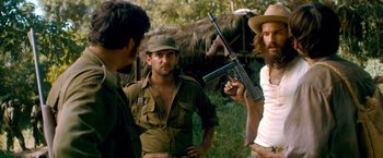 Movie still from “Che: Part One” (2008), directed by Steven Soderbergh – A group of men standing next to each other holding guns; Medium shot, Over the shoulder angle