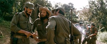 Movie still from “Che: Part One” (2008), directed by Steven Soderbergh – A man with a beard is talking to a man with a hat on; Medium shot, Over the shoulder angle