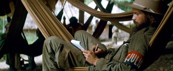 Movie still from “Che: Part One” (2008), directed by Steven Soderbergh – A man sitting in a hammock writing in a notebook; Medium shot, High angle