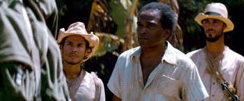 Movie still from “Che: Part One” (2008), directed by Steven Soderbergh – Two men standing next to each other near a tree; Medium shot, Low angle