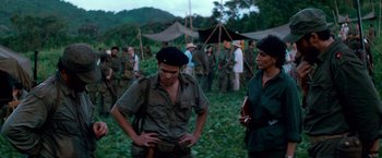 Movie still from “Che: Part One” (2008), directed by Steven Soderbergh – A group of people standing in the grass; Medium shot, Over the shoulder angle