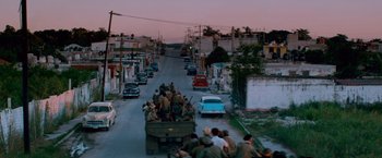 Movie still from “Che: Part One” (2008), directed by Steven Soderbergh – A truck full of people driving down a street; Extreme Wide shot, High angle