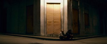 Movie still from “Che: Part One” (2008), directed by Steven Soderbergh – Two people sitting on the ground in front of a building; Wide shot, High angle