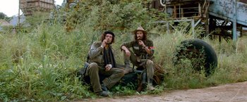 Movie still from “Che: Part One” (2008), directed by Steven Soderbergh – A couple of men sitting next to each other on some grass; Medium shot, Over the shoulder angle