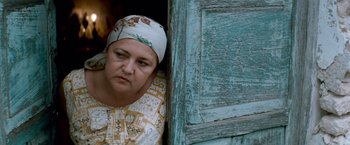 Movie still from “Che: Part One” (2008), directed by Steven Soderbergh – An older woman wearing a head scarf is leaning against a door; Close Up shot, Low angle