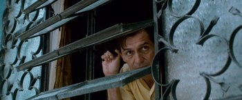 Movie still from “Che: Part One” (2008), directed by Steven Soderbergh – A man leaning on a metal fence with one hand up to his ear; Close Up shot, Low angle