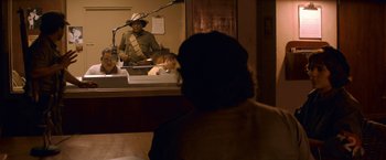 Movie still from “Che: Part One” (2008), directed by Steven Soderbergh – A man sitting in front of a microphone in front of a woman; Medium shot, Over the shoulder angle