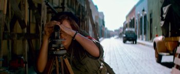 Movie still from “Che: Part One” (2008), directed by Steven Soderbergh – A woman taking a picture with a camera on the street; Medium shot, High angle